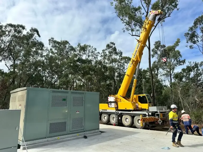 A crane lifting equipment on a high-voltage installation site surrounded by trees, with workers wearing safety gear overseeing the operation – GAP Industries project.